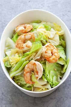 a white bowl filled with lettuce and shrimp on top of a gray surface