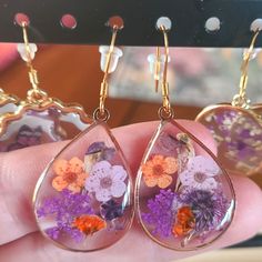 Orange And Purple Pressed Flowers In Resin. Teardrop Shaped Frame. Gold Frame And 18k Gold Plated Stainless Steel Earwires. Comes With Earring Backs, An Earring Card And A Mesh Bag For Storage. Lightweight. Purple Dangle Teardrop Earrings Gift, Purple Pressed Flower Earrings For Gift, Purple Pressed Flower Earrings Gift, Purple Pressed Flower Drop Earrings, Purple Pressed Flower Earrings, Purple Birth Flower Drop Earrings, Sparrow Jewelry, Flowers In Resin, Earring Card