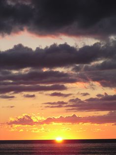 the sun is setting over the ocean with dark clouds