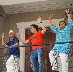 two men and a woman are standing on the balcony with their arms in the air