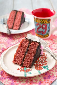 two slices of red velvet cake on plates next to a cup of tea and fork