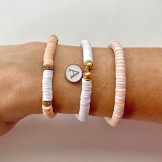 This classy peach and white heishi beaded bracelet set comes with gold accents to further give it a luxe look.  You have the option to purchase style 1-3 bracelets or purchase the whole set. Please refer to the picture marked style 1, 2, & 3 for a visual on each bracelet. (Also listed out below)  Quick Specs:  + 3 Styles all on durable stretch Bands. + Style 1: Peach and white heishi with rhinestone ring accents. + Style 2: White heishi with gold accents and a letter charm of choice. + Style 3: Orange Heishi Beads Jewelry For Friendship, White Stackable Heishi Beads Jewelry, White Beaded Bracelets With Gold Beads For Friendship, White Heishi Beads Bracelet With Gold Beads, Letter Bracelet, Stretch Bands, Rhinestone Ring, Heishi Beads, Name Bracelet