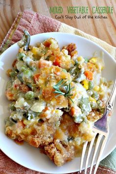 a white plate topped with casserole covered in vegetables and sauce next to a fork