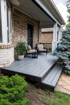 a wooden deck in front of a house with two chairs and plants on the side