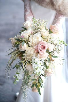 a bridal bouquet with white flowers and greenery is held by a fur stoler