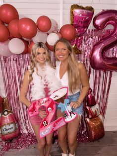 two women standing next to each other in front of balloons and streamers with numbers on them