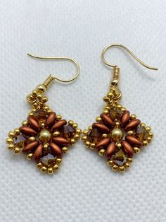 two pairs of gold and brown beaded earrings on white fabric with beads in the shape of flowers