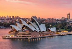 the sydney opera house is lit up at sunset