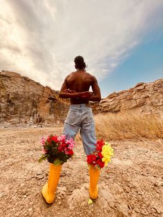 a man standing on top of a dirt field with flowers in yellow rubber booties