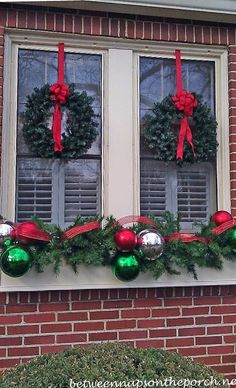 two christmas wreaths are hanging on the window sill in front of a brick building