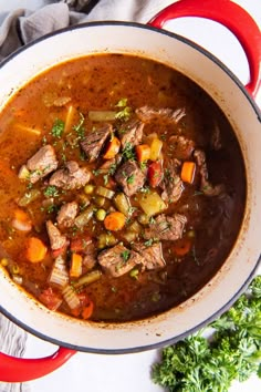 a red pot filled with beef and vegetable soup on top of a white tablecloth