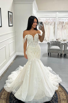 a woman in a wedding dress taking a selfie with her cell phone while standing on a rug