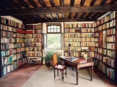 a room filled with lots of books next to a table and chair in front of a window