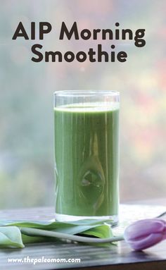 a glass filled with green smoothie sitting on top of a table next to tulips