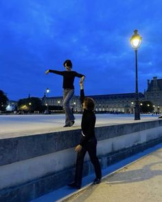 two people standing on the edge of a stone wall near a street light at night