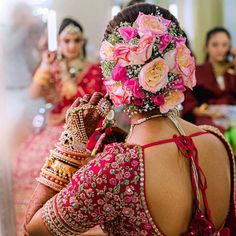 the back of a woman's head with pink flowers in her hair and jewelry