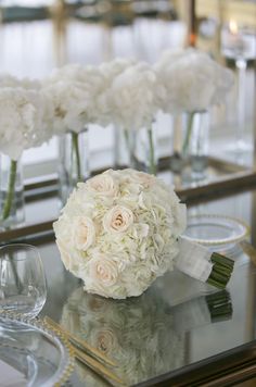 flowers in vases are sitting on a glass table with wine glasses and silverware