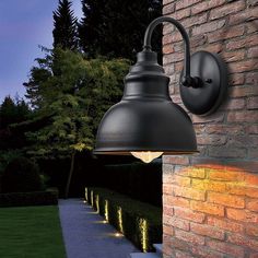 an outdoor light on the side of a brick wall next to a walkway and trees