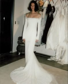 a woman in a white dress standing next to a rack with dresses on hangers