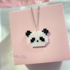 a cross stitch panda bear necklace on a pink card