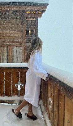 a woman walking in the snow on top of a wooden fence next to a building