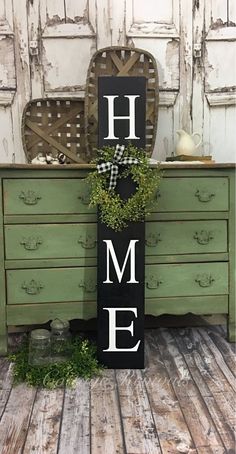 a sign that says home on it sitting in front of a dresser with a potted plant