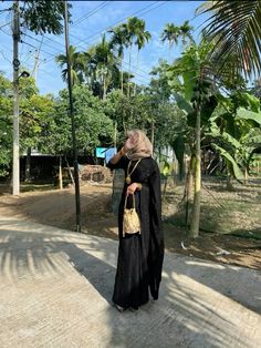 a woman standing on the side of a road next to palm trees and power lines