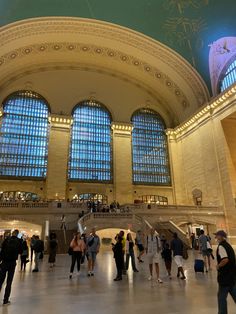 many people are standing in the lobby of a large building with high ceilings and arched windows