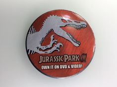 a red and white button with a dinosaur on it's side that says, jurassic park