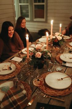 two women sitting at a table with plates and place settings in front of them, lit by candles