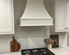 a stove top oven sitting inside of a kitchen next to white cabinets and wooden cutting boards