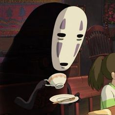 two people sitting at a table with food in front of them and a mask on the wall behind them