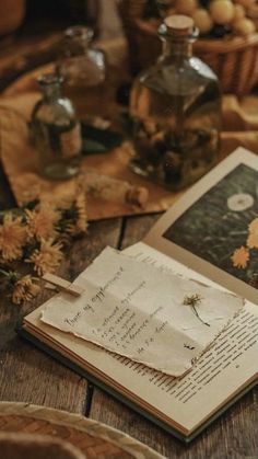 an open book sitting on top of a wooden table next to some flowers and jars