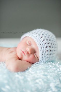 a baby wearing a crochet hat laying on top of a blue blanket with his eyes closed