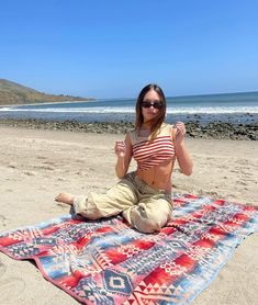 a woman sitting on top of a beach next to the ocean holding her fist up