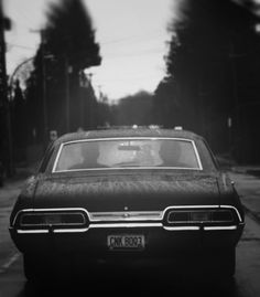 a black and white photo of a car parked on the side of the road with trees in the background