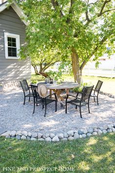 a table and chairs sitting on gravel in front of a tree with rocks around it