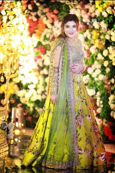 a woman in a yellow and green outfit standing next to flowers on the wall with lights