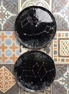 two black plates sitting on top of a tile floor covered in stars and moon designs