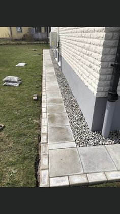 the side of a house with grass and rocks on it, next to a sidewalk