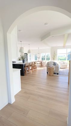 an open living room and kitchen area with white walls, hardwood flooring and large arched doorway