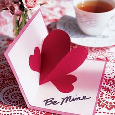 a valentine's day card with a paper heart on it next to a cup of tea