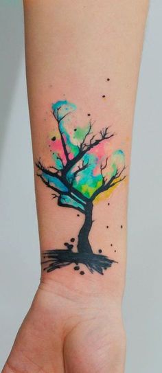 a tree tattoo on the arm with watercolor paint splatters all over it