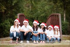 a group of people sitting on top of a wooden bench wearing santa's hats