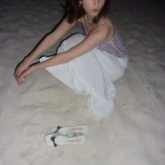 a woman sitting in the sand with her skis on the ground next to her