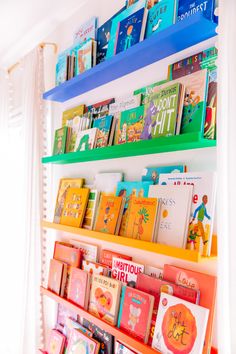 colorful bookshelves in a child's room with white curtains and window behind them