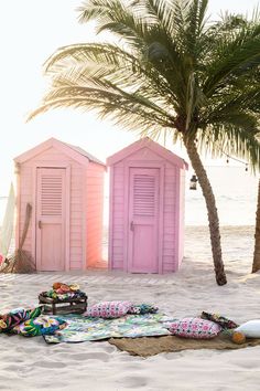 two pink beach huts sitting next to each other on top of a sandy beach under a palm tree