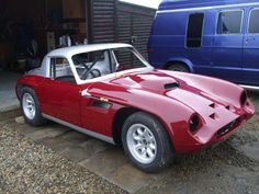 a red and white sports car parked in front of a blue van next to another vehicle