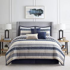 a bed with blue and white comforters in a room next to a painting on the wall