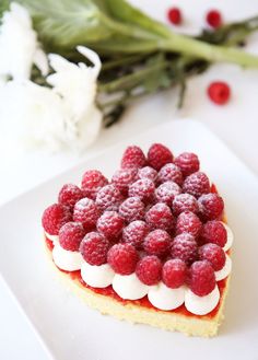 a heart shaped cake topped with raspberries on top of a white square plate